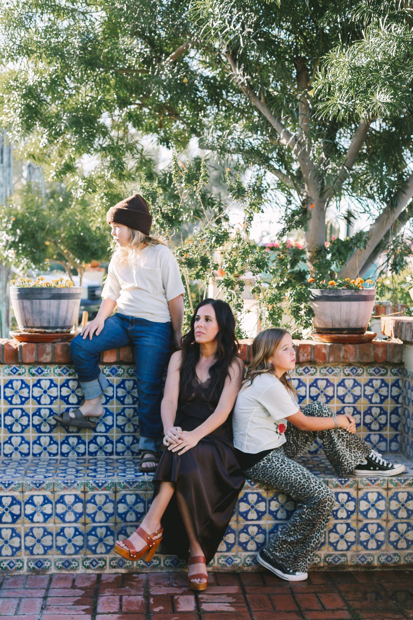 Mother sitting on tiled steps with two children in sunny outdoor garden setting.