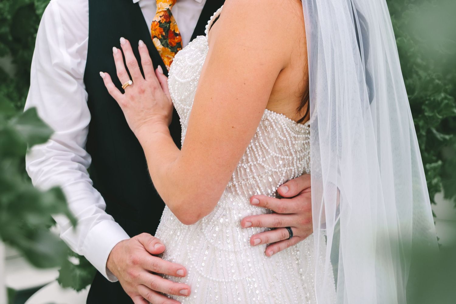 Close-up of bride and groom embracing, showcasing beaded wedding gown and wedding rings.