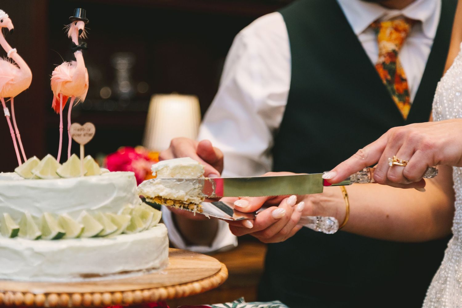 Bride and groom cutting white wedding cake topped with pink flamingo decorations at reception.