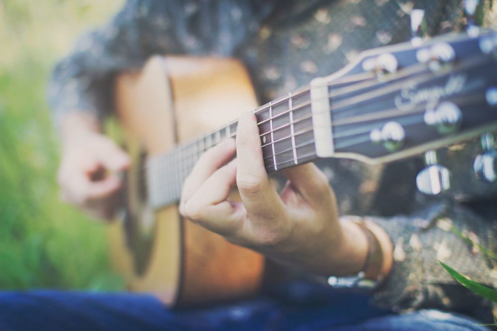 Close-up of hands playing acoustic guitar strings outdoors in natural setting.