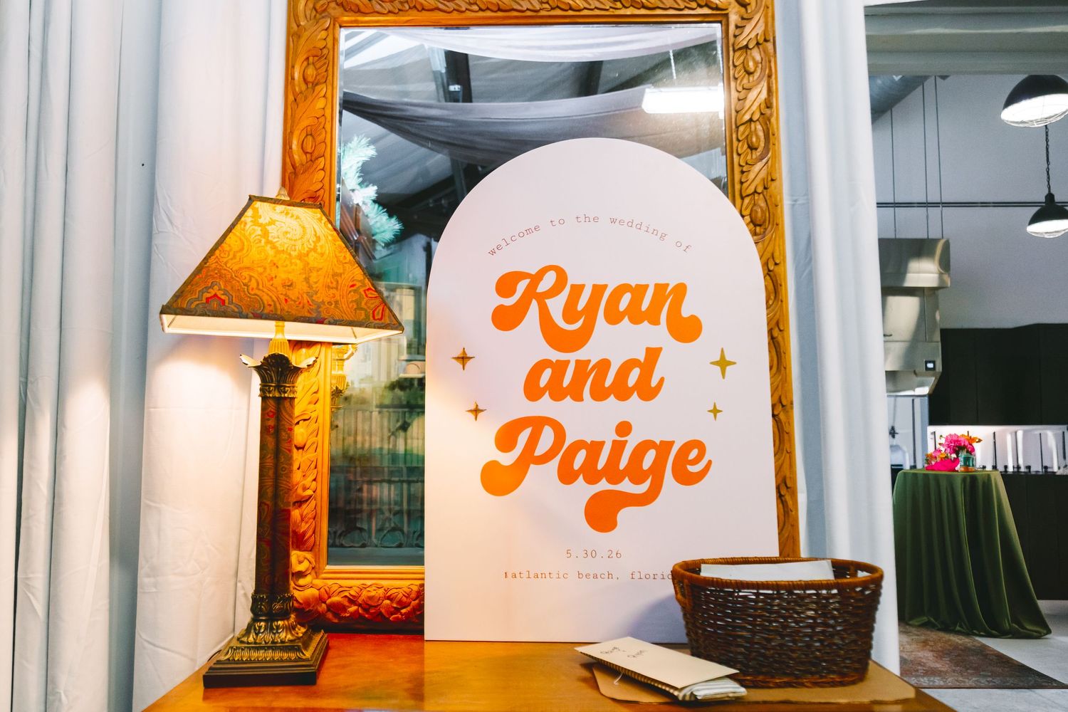 Retro-style Ryan and Paige wedding welcome sign in orange on white arch with gold mirror.