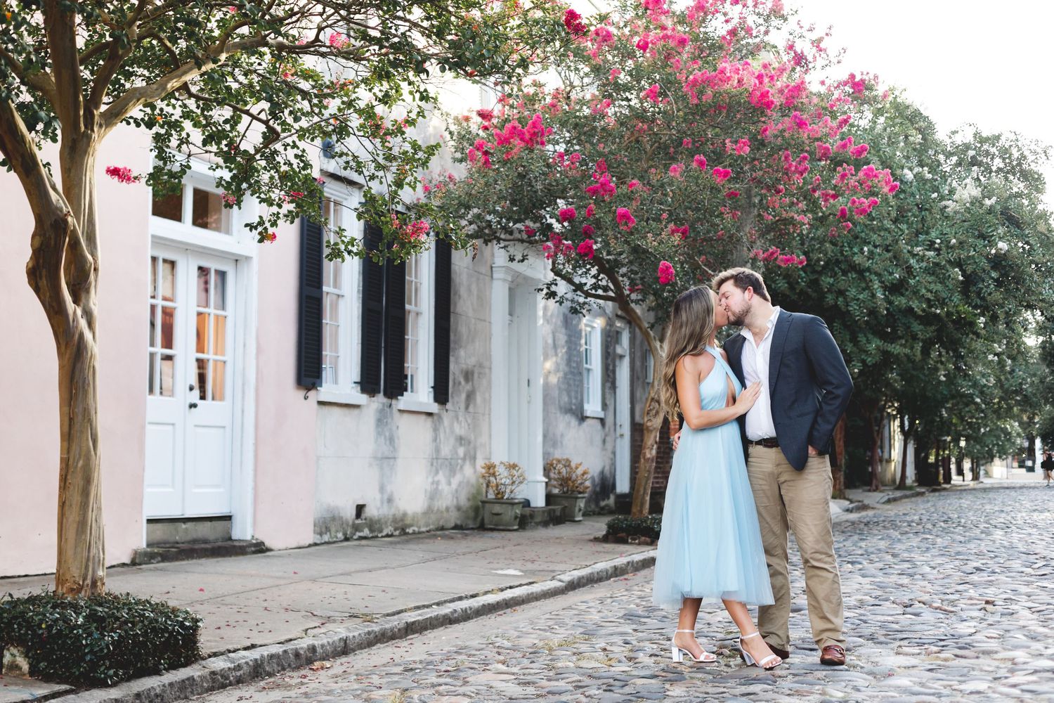 Couple sharing a kiss on a cobblestone street lined with colorful historic homes.