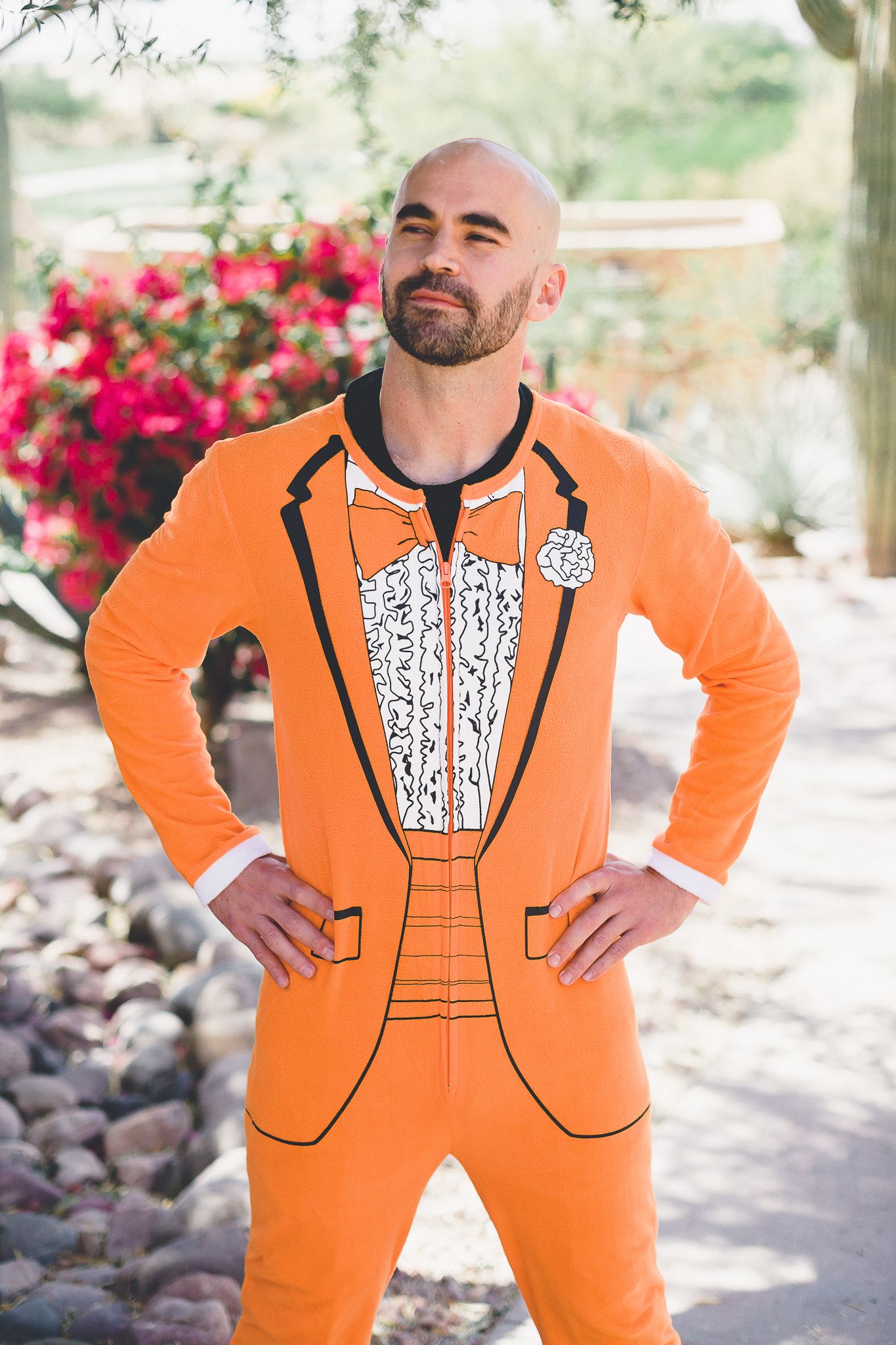 Confident bald man with beard wearing a bold orange tuxedo jumpsuit outdoors.