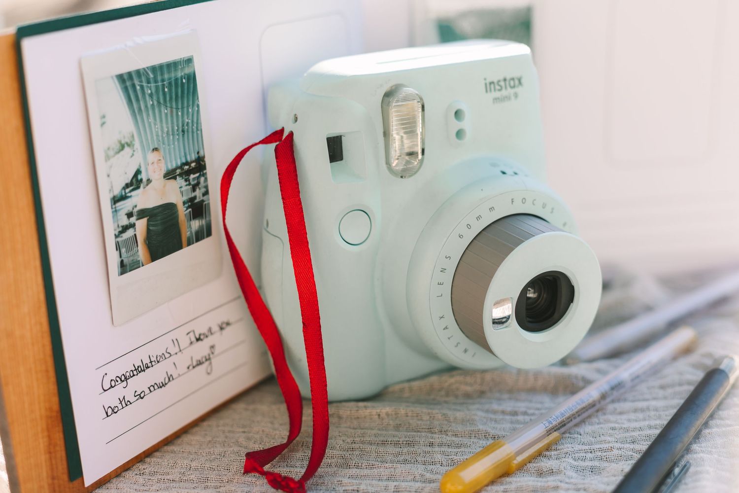 Fujifilm Instax Mini camera with red strap rests on wedding guest book beside gold pen.