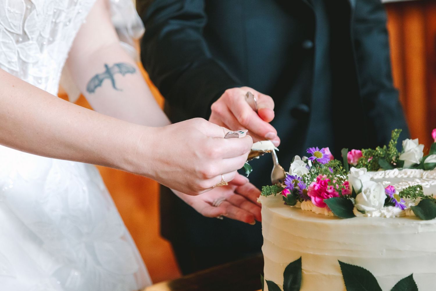 Bride and groom cutting their floral-decorated wedding cake together during reception celebration.