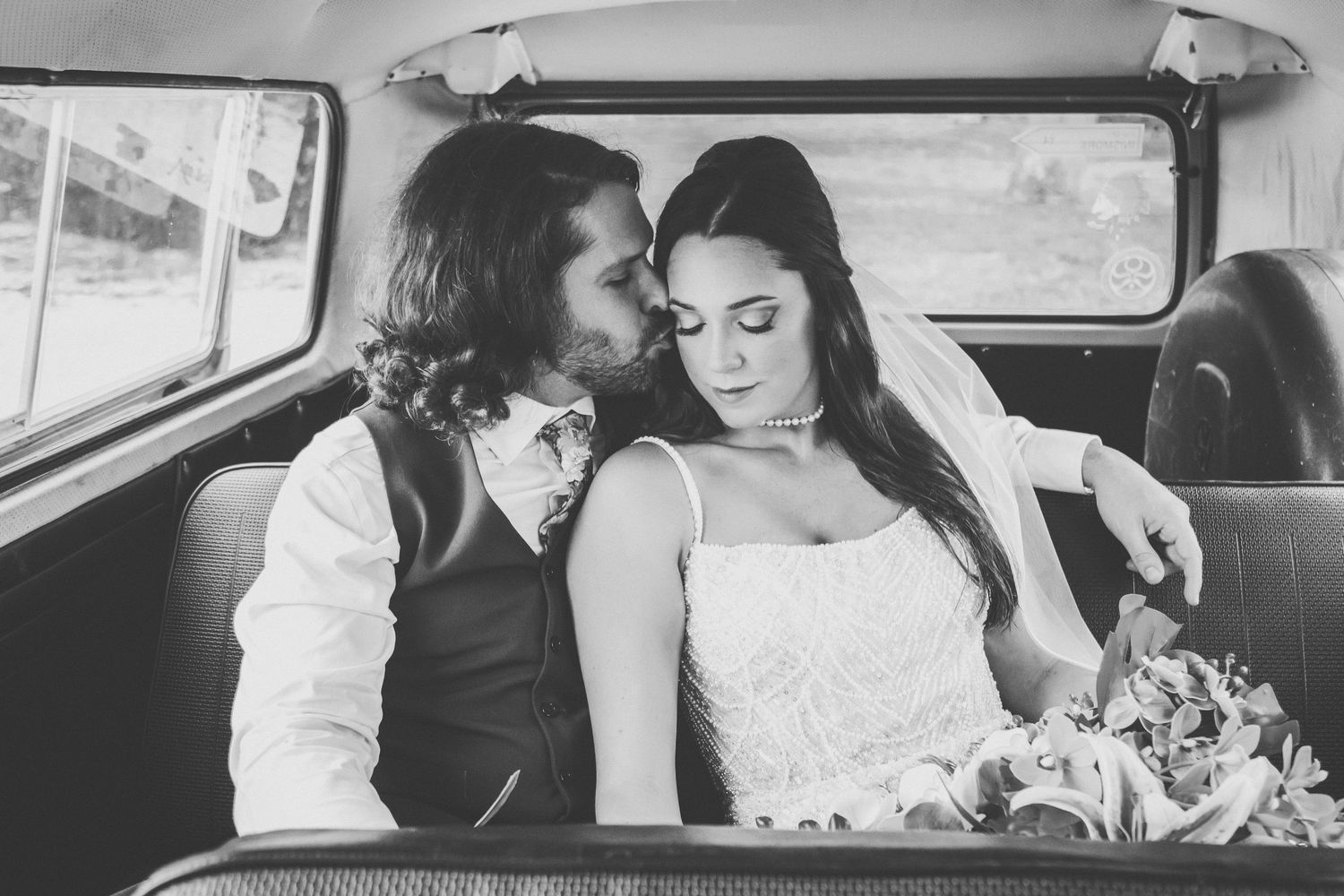 Black and white photo of bride and groom sharing intimate moment in vintage car backseat.