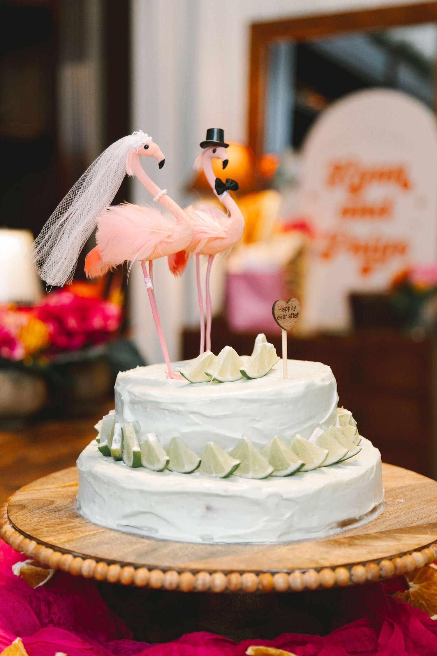 Two-tier white wedding cake topped with flamingo bride and groom figurines at a vibrant wedding.