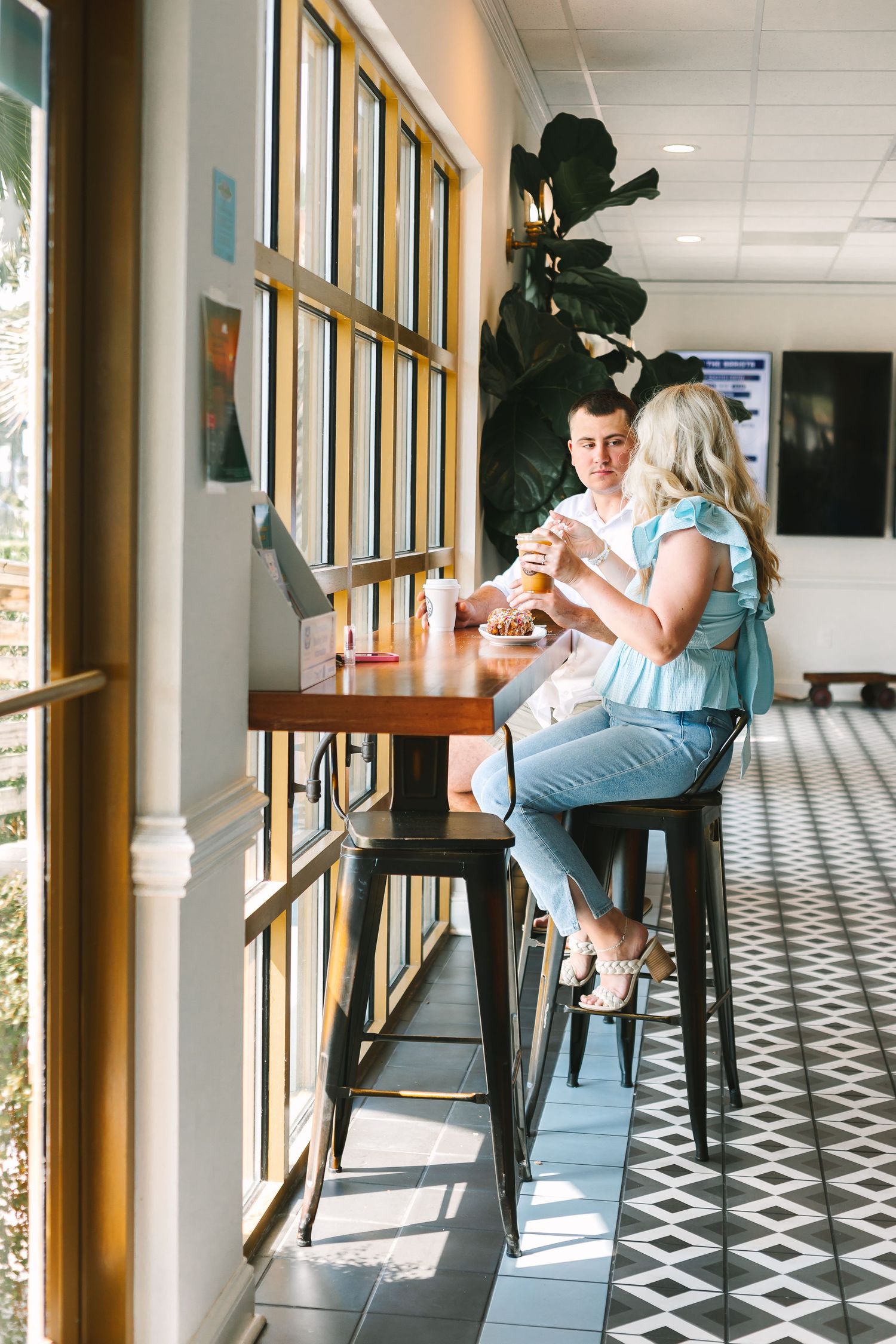 Young couple sharing ice cream at a bar-height table in a bright cafe.
