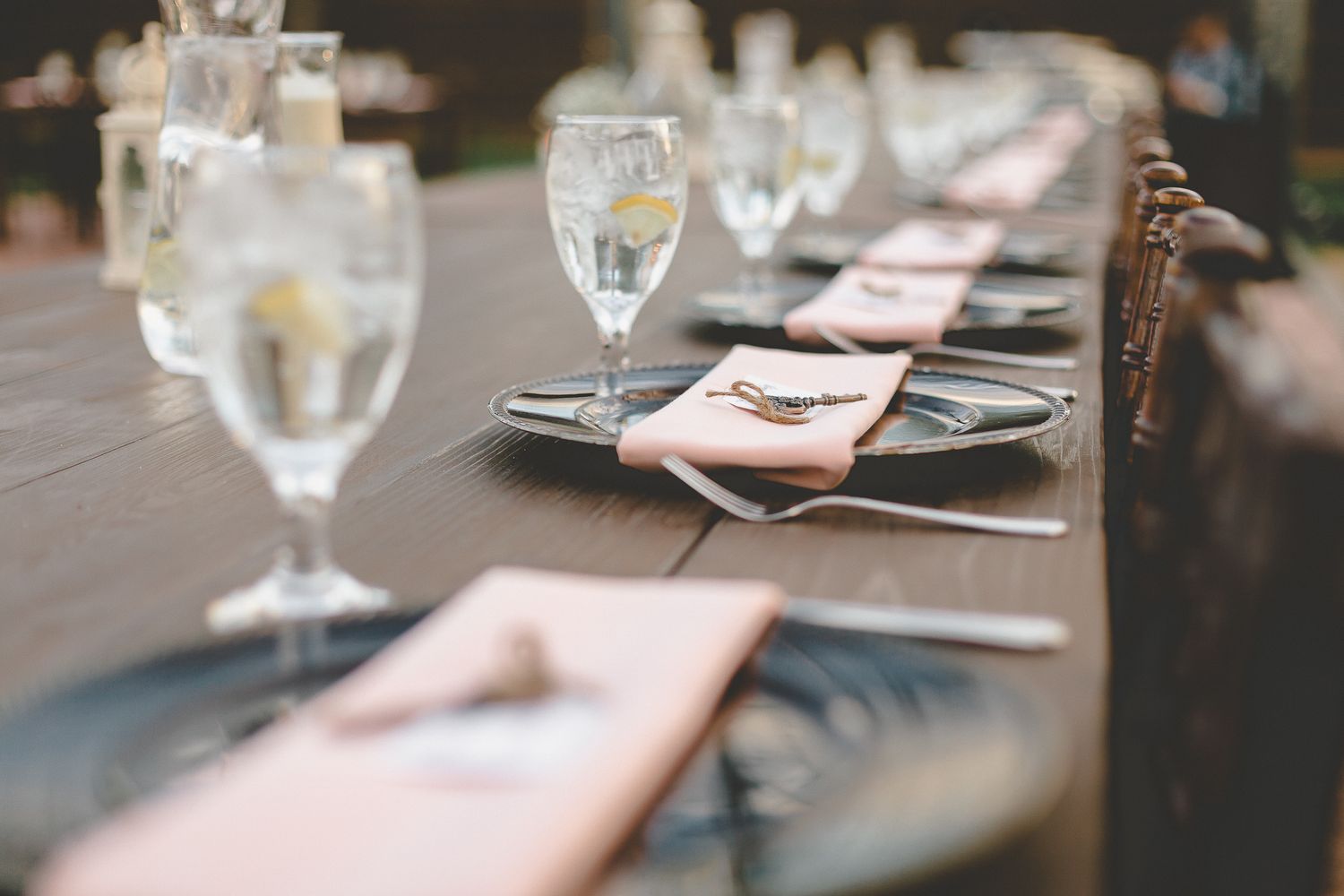 Elegant wedding reception table setting with pink napkins, gray plates, and crystal glassware.