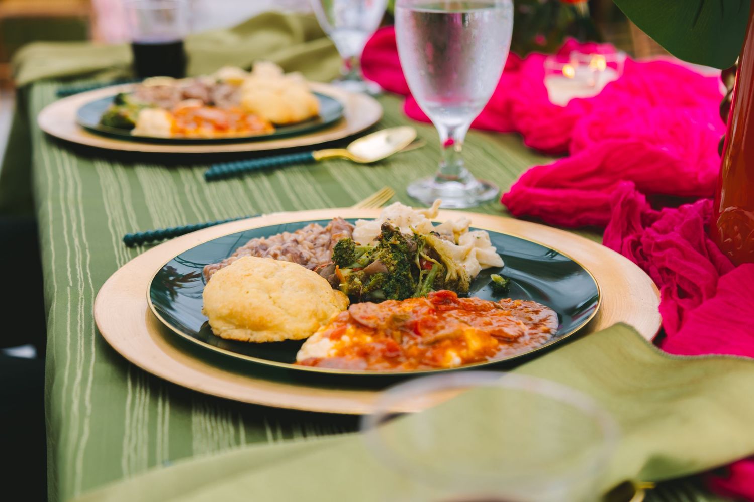 Wedding reception dinner plate with lasagna, cornbread, and greens on green tablecloth.