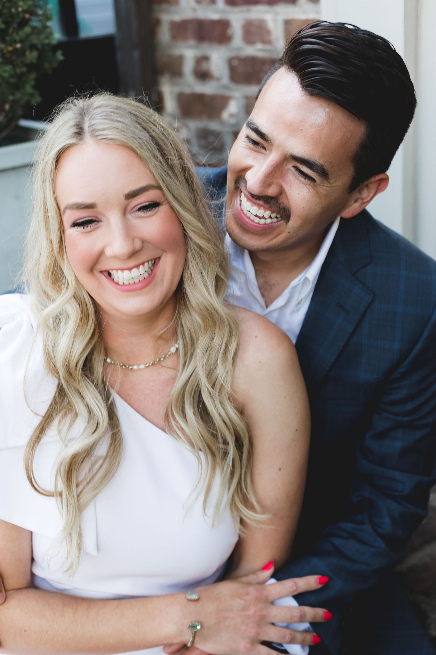 Smiling blonde woman and dark-haired man laughing together during an engagement photo session.