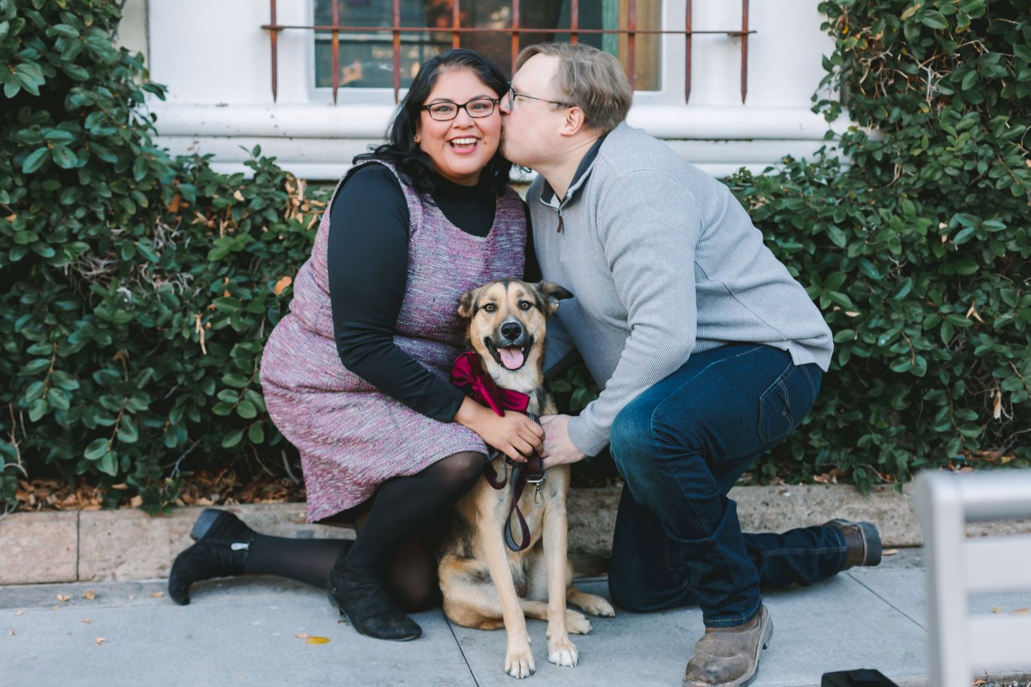 Couple sharing a kiss with their happy smiling dog during an outdoor engagement photo session.