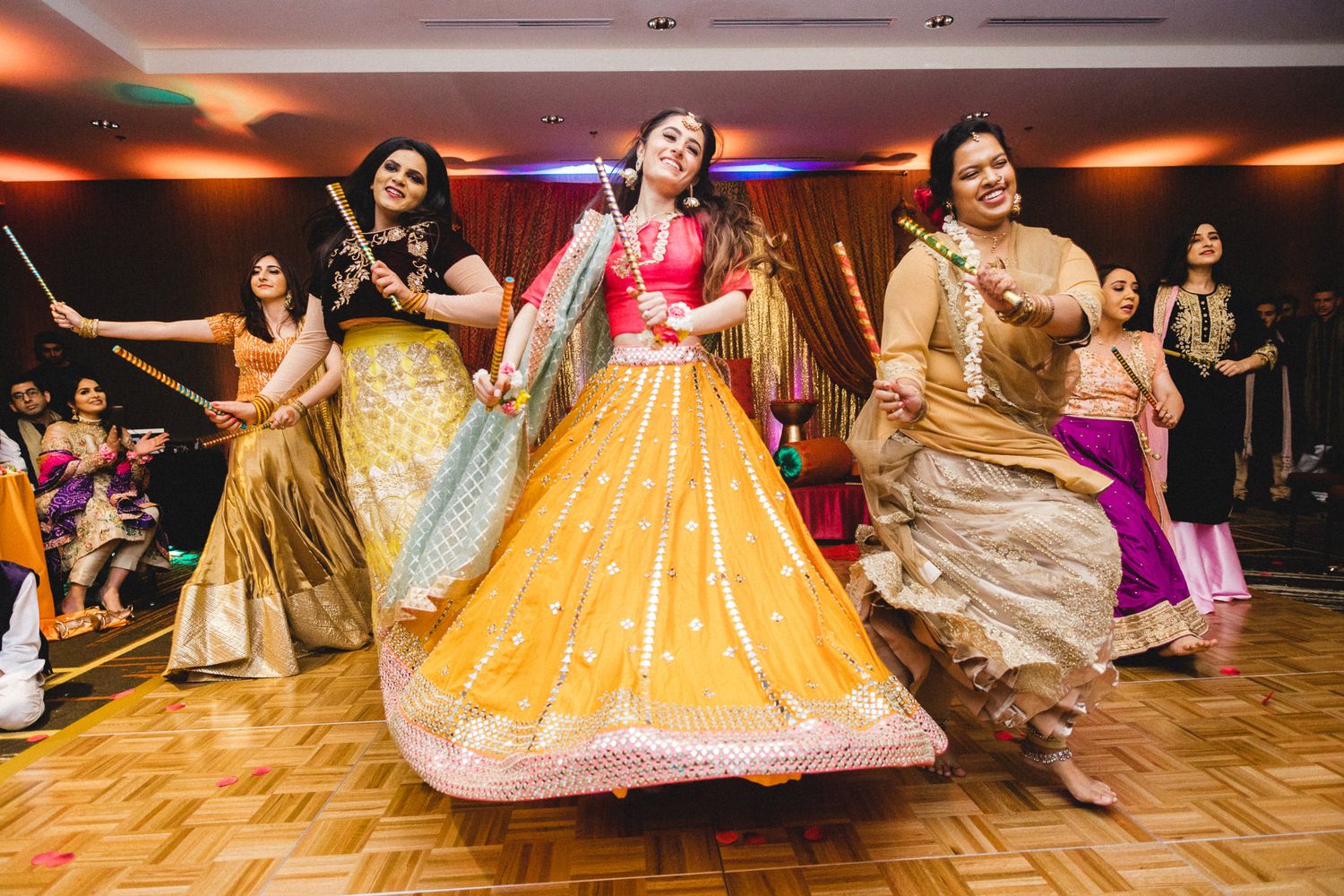 Indian women dancing energetically in colorful lehengas during traditional wedding sangeet celebration.