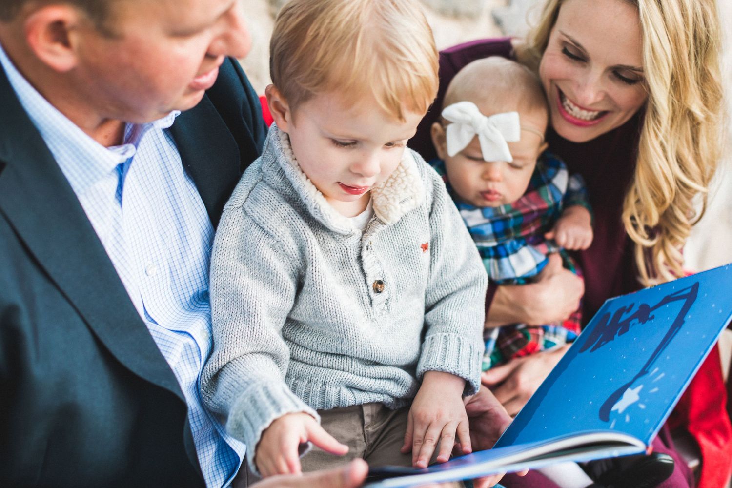 Happy family reading colorful book together with toddler and baby girl with bow headband.