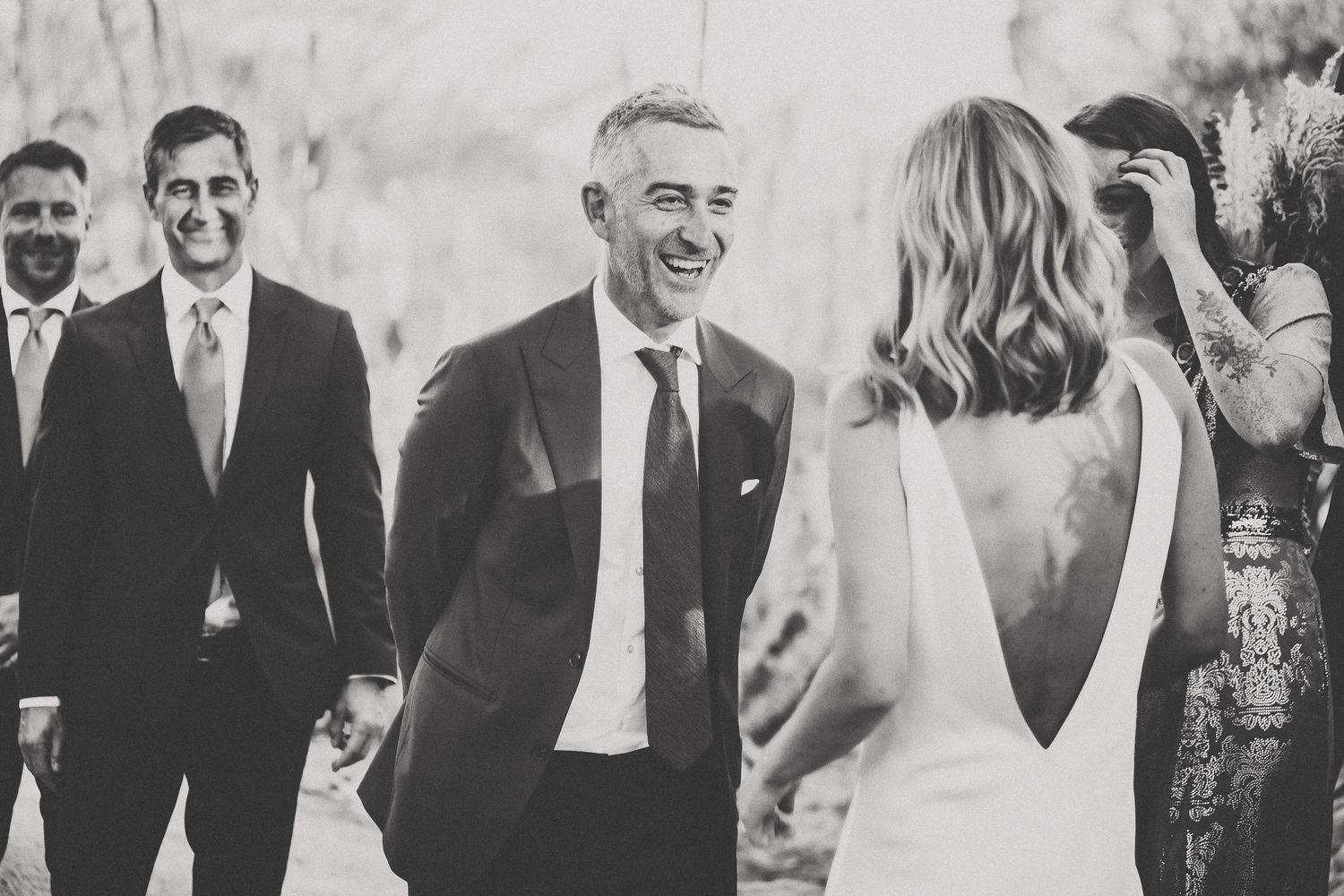 Black and white photo of a groom laughing joyfully with wedding guests during the ceremony.