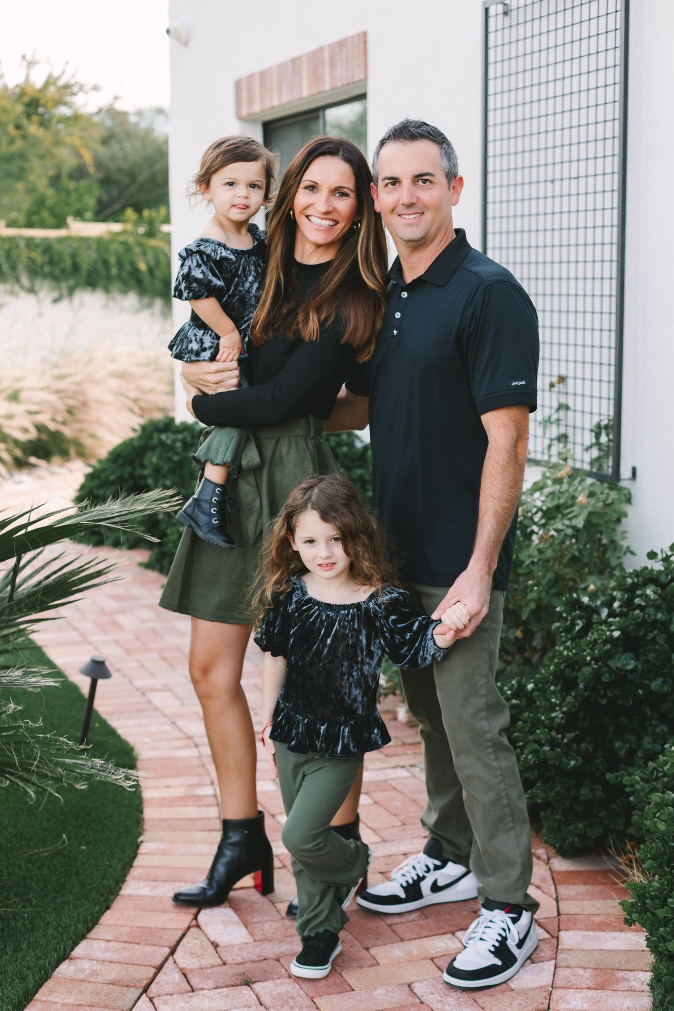 Family of four posing on a brick path in a garden, dressed in coordinating black and green outfits.