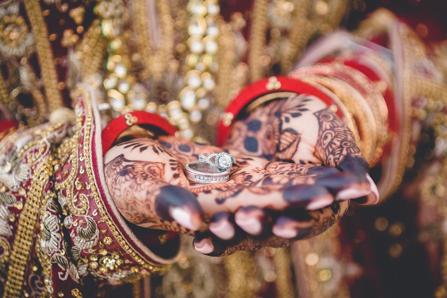 Bride with intricate mehndi henna hands holding wedding rings at Indian ceremony.