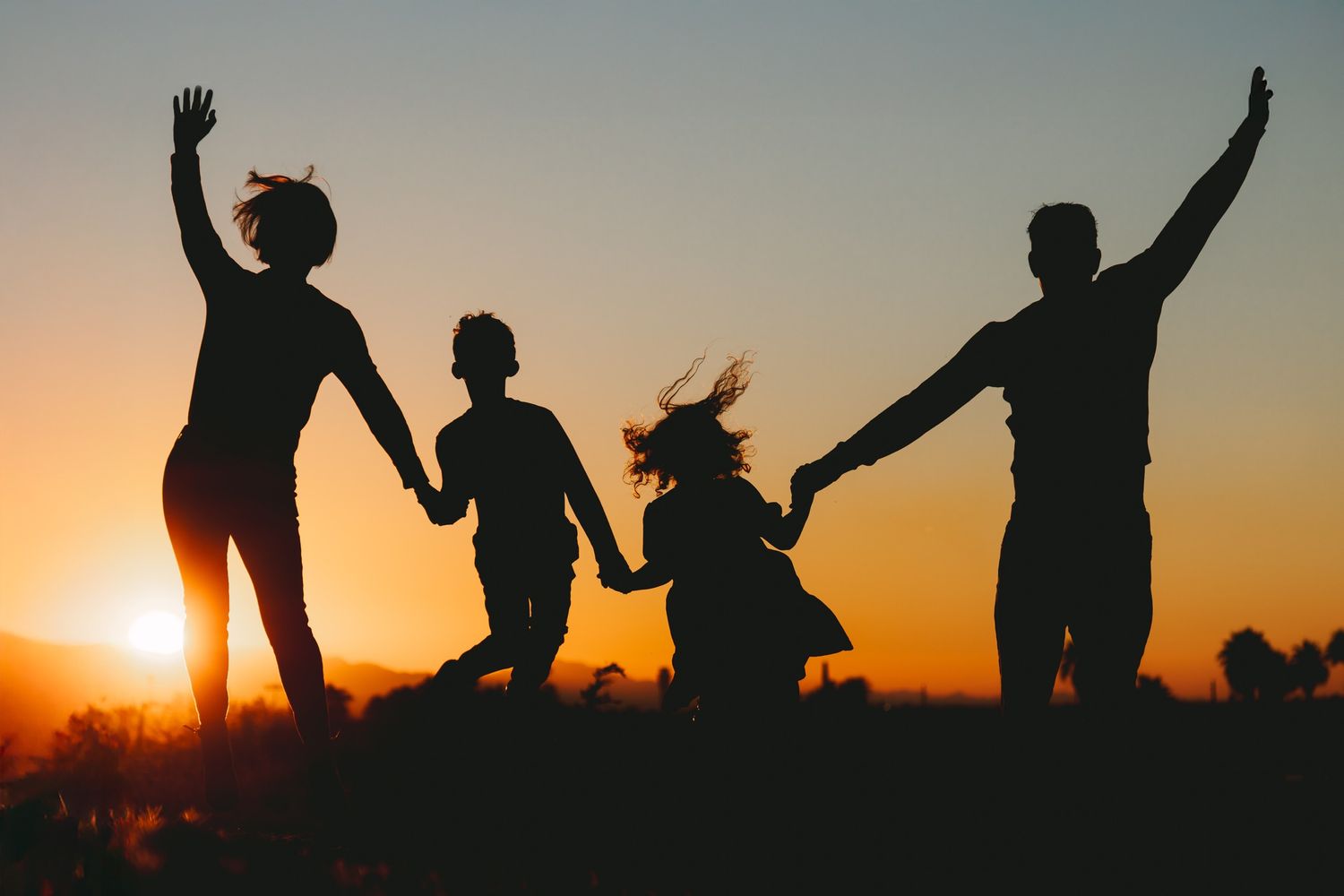 Silhouette of four people jumping with raised arms against vibrant golden sunset sky.