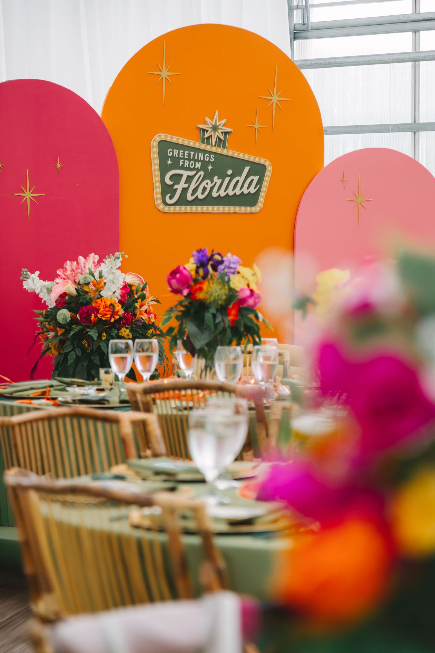 Colorful Florida-themed wedding reception with vibrant floral centerpieces and retro Greetings from Florida sign backdrop.