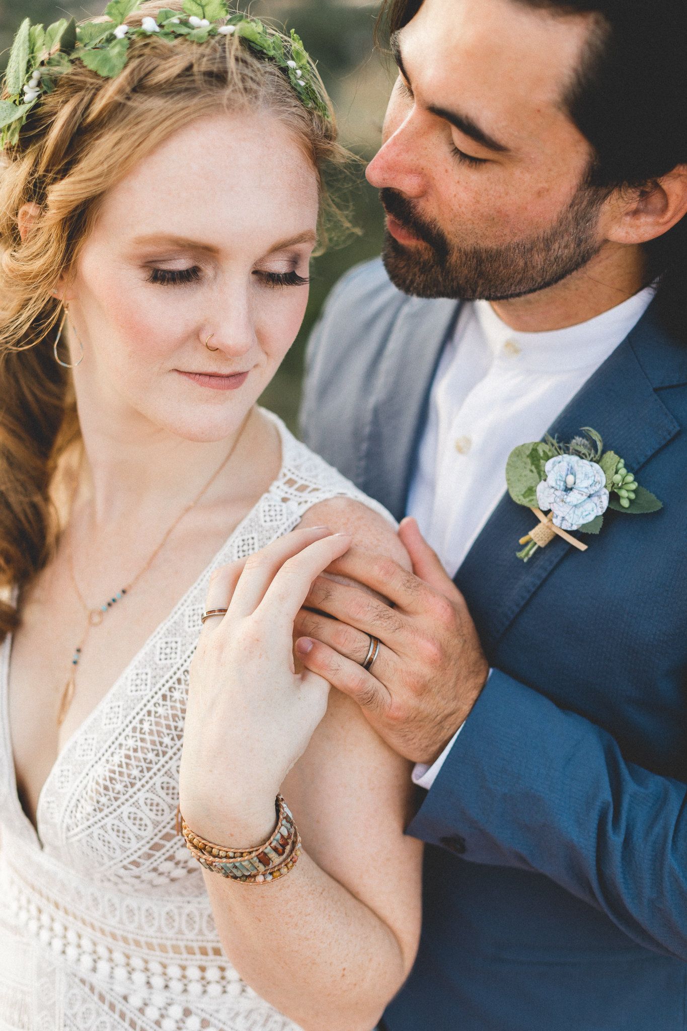 Groom tenderly holding brides hand as she wears floral crown at boho wedding.