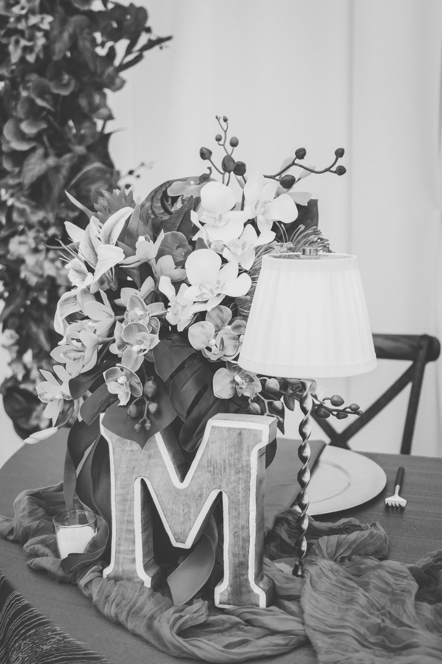 Black and white wedding table centerpiece with orchids, letter M, small lamp, and elegant floral arrangement.