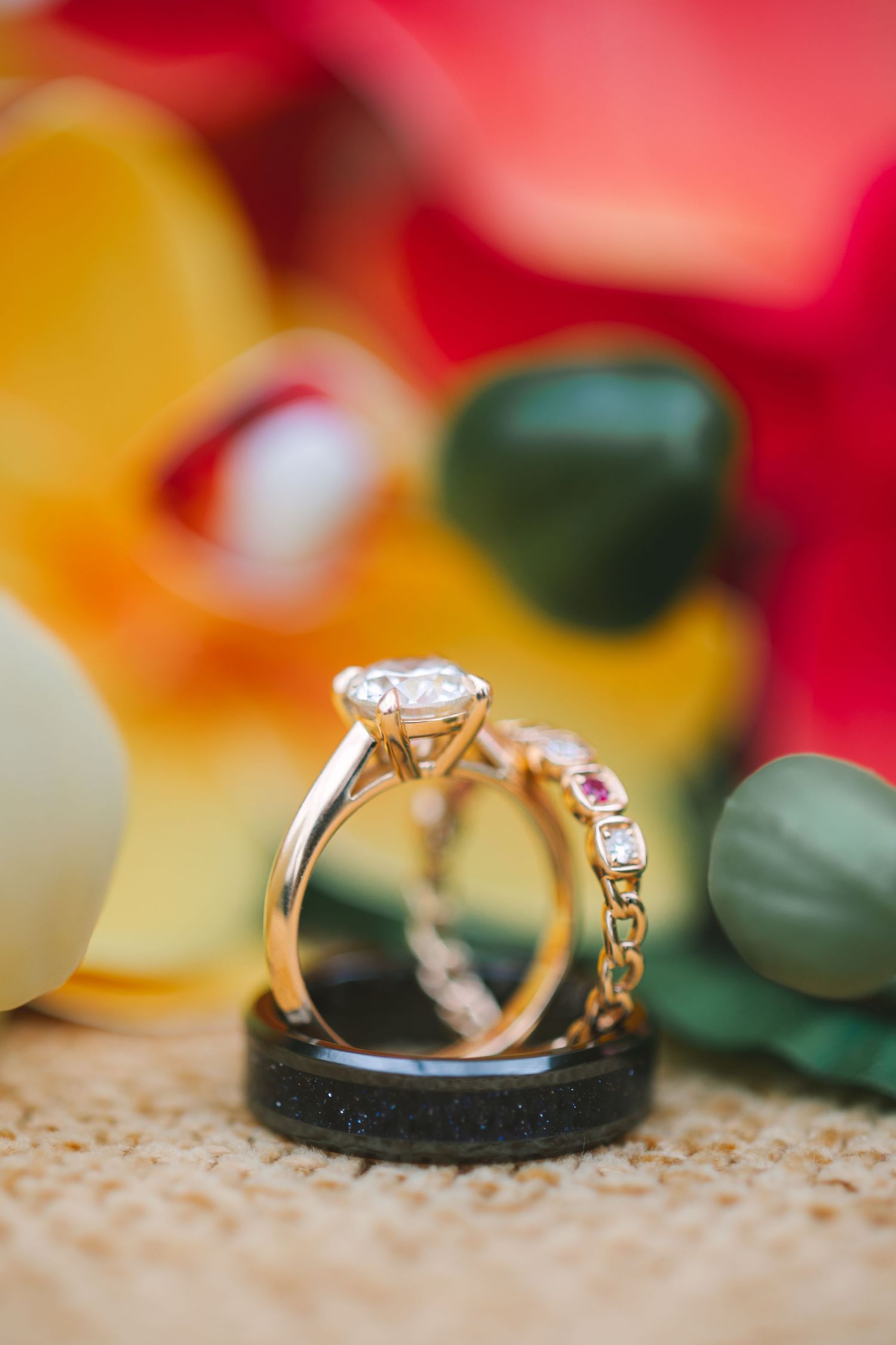 Gold solitaire diamond engagement ring paired with a delicate pink gemstone band displayed on a dark ring holder.