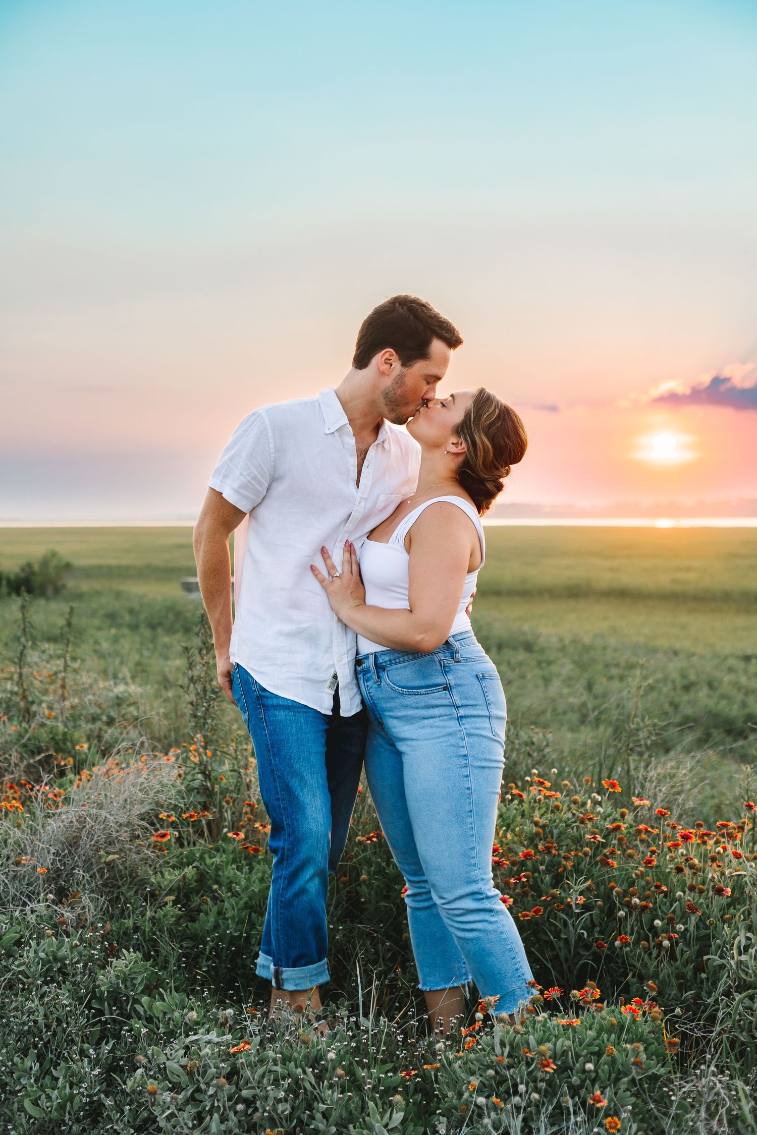 Couple sharing a romantic kiss in a field of wildflowers at sunset.