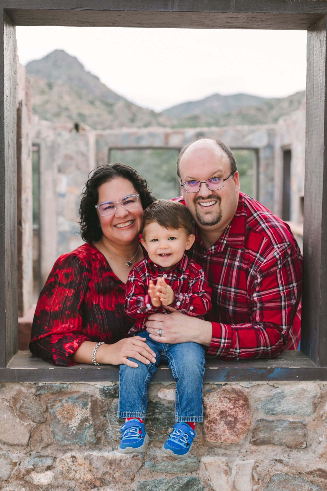 Happy family of three in matching red outfits posing with toddler at a scenic rocky outdoor location.