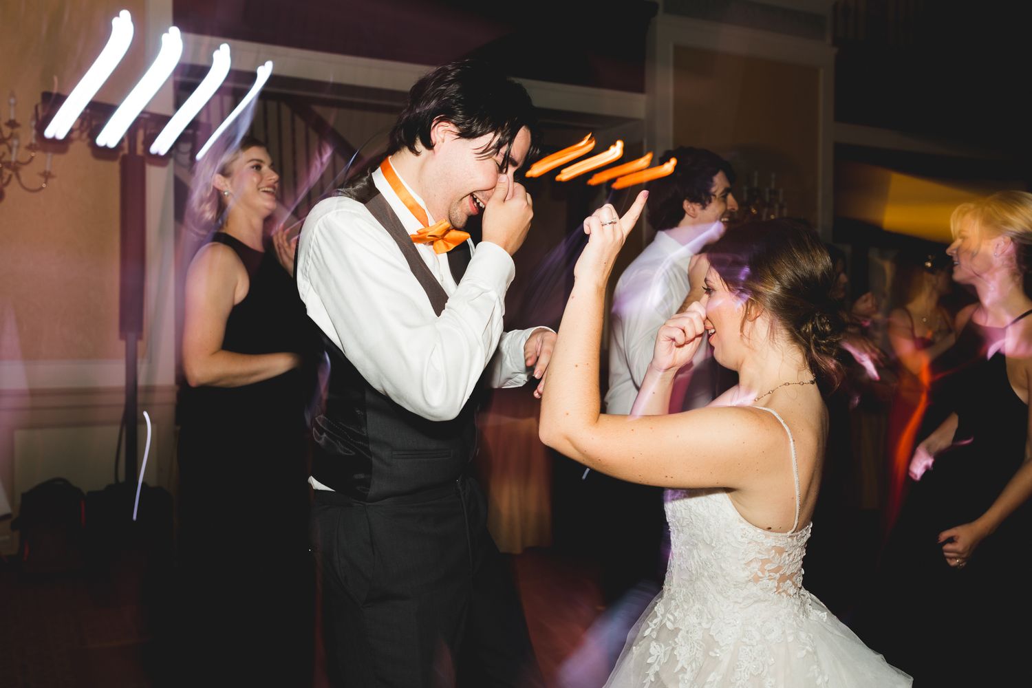 Bride and groom share a fun dance moment under colorful lights at reception.