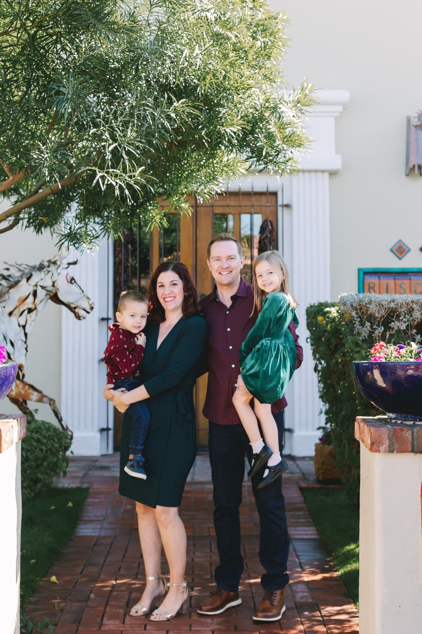 Smiling family of four with two young children pose outside elegant home entrance.