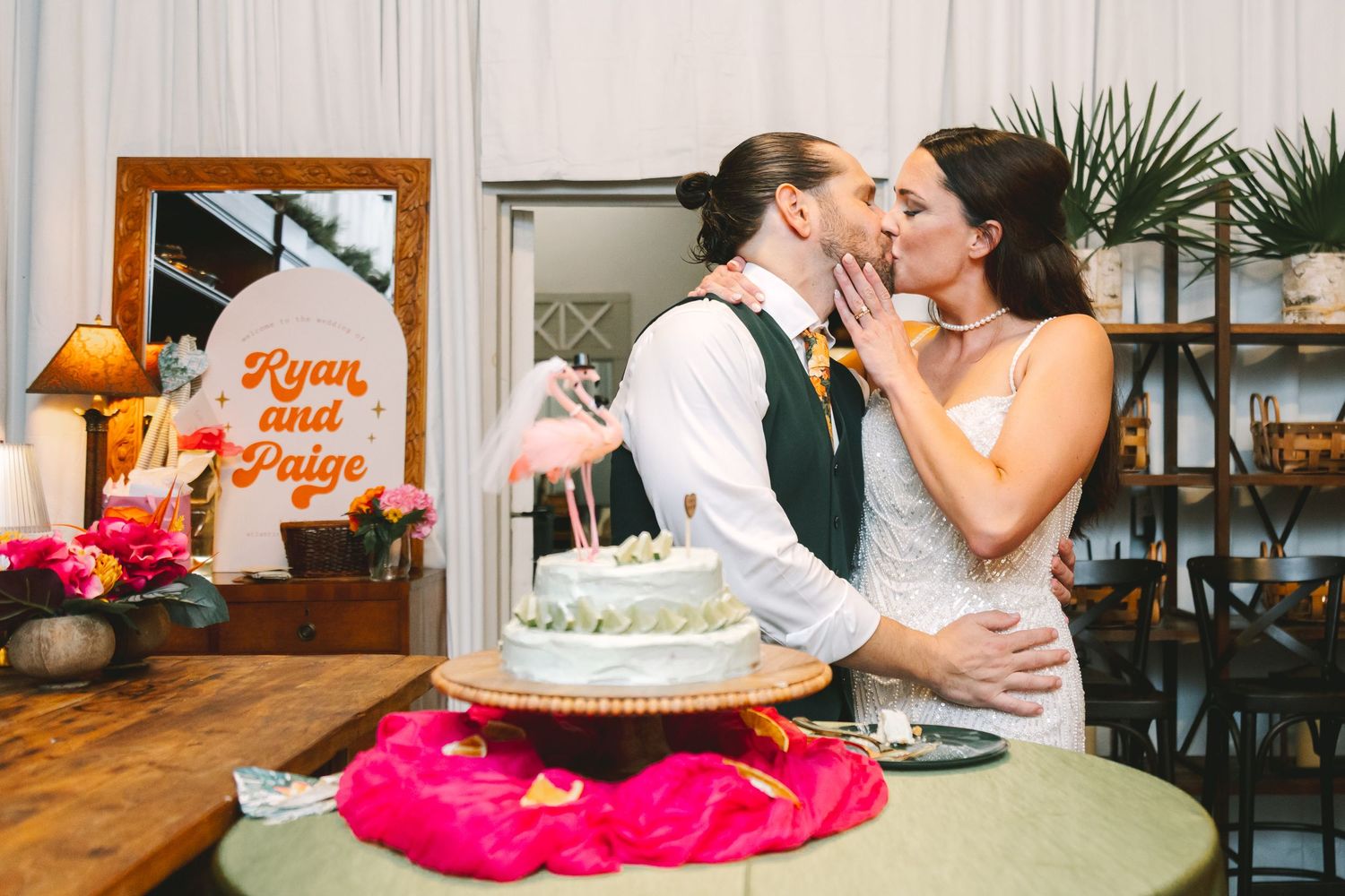 Bride and groom kissing behind wedding cake near Ryan and Paige wooden sign at reception.