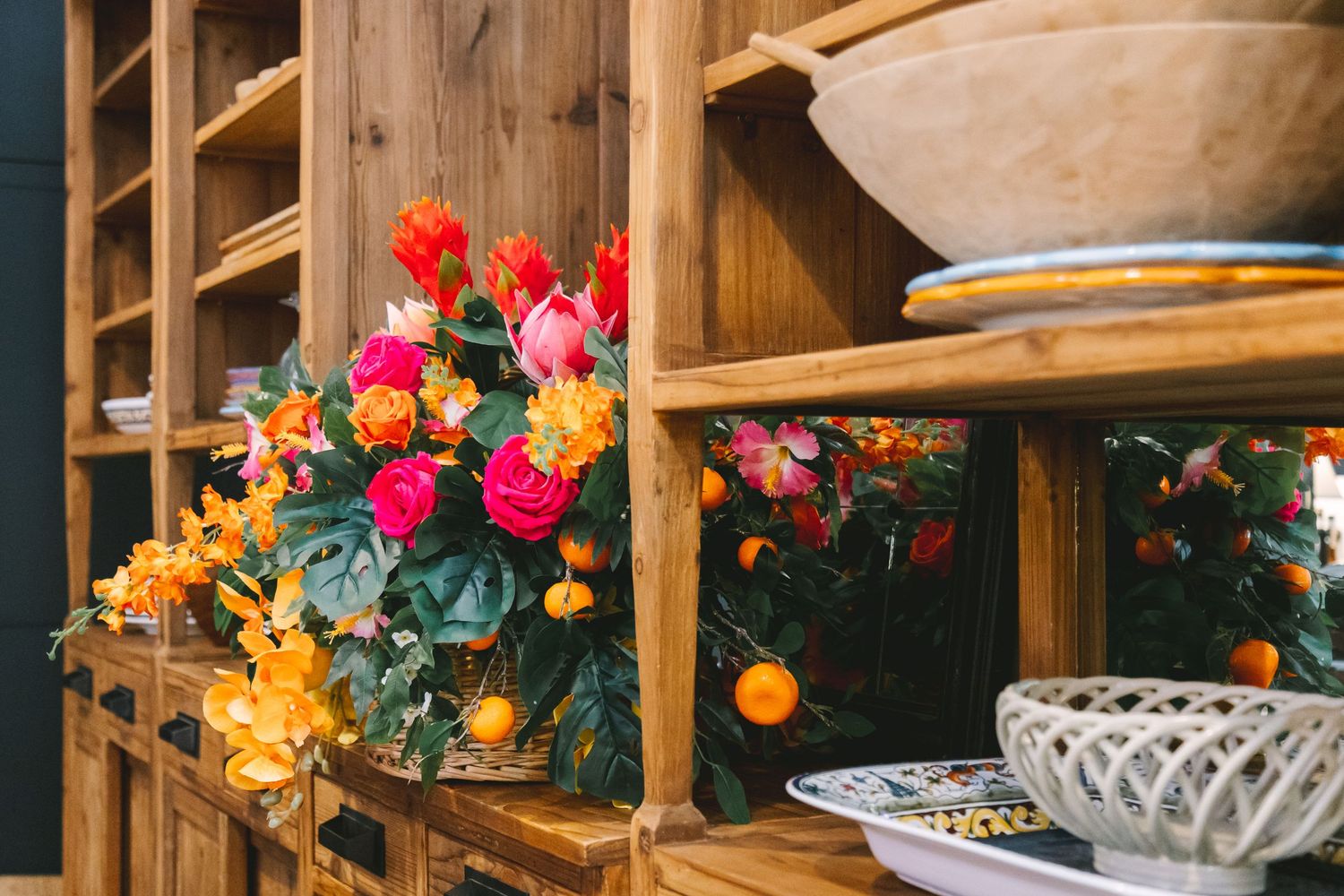 Wooden shelving display with vibrant orange and pink floral arrangements and decorative plates.