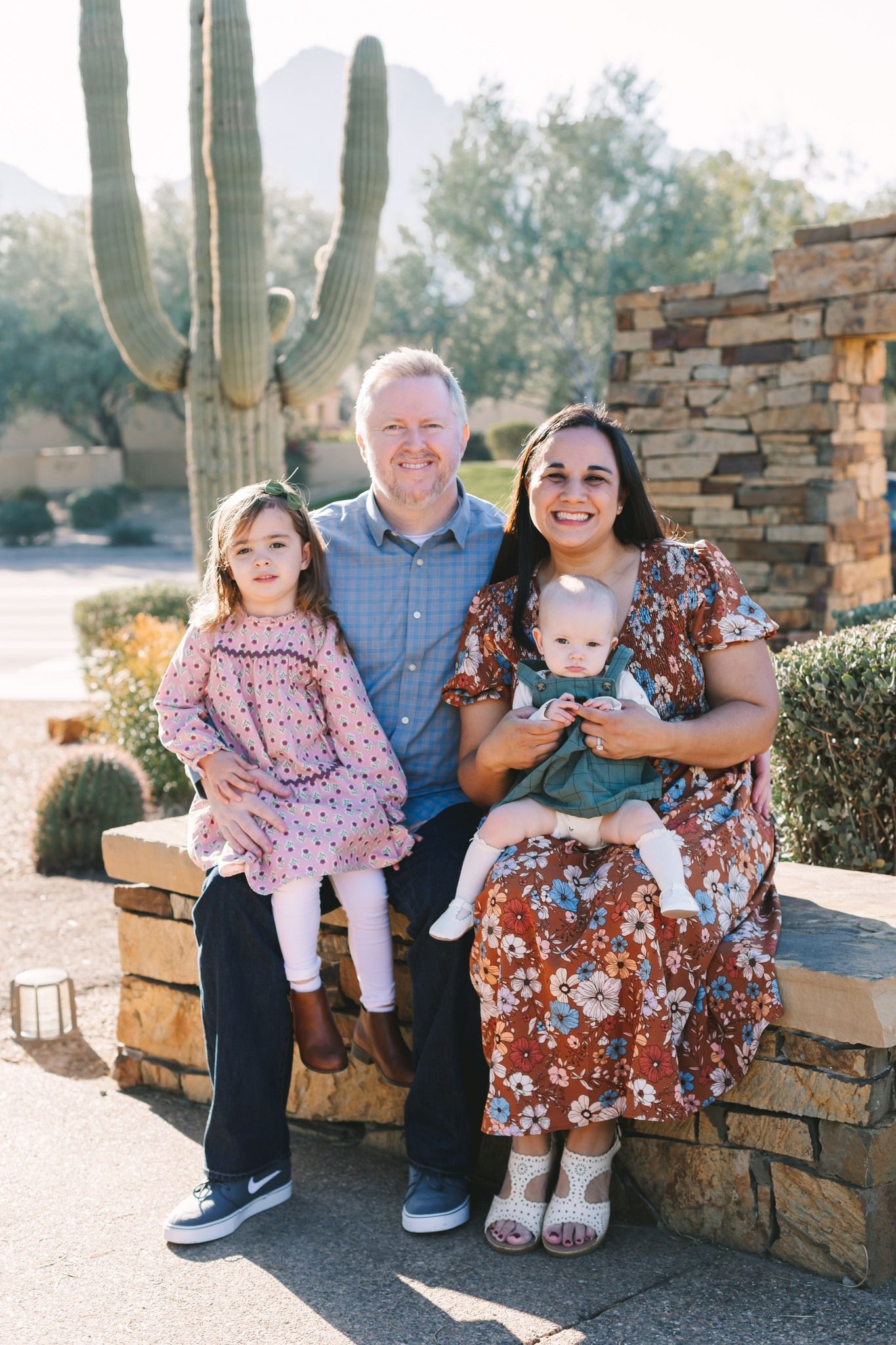 Family of four sitting on a stone wall outdoors with a tall saguaro cactus in the background.
