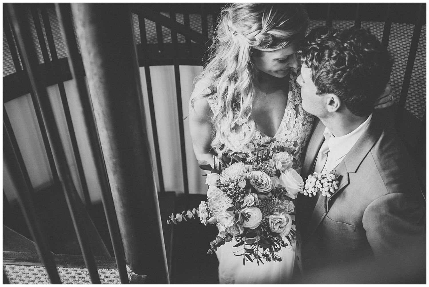 Black and white photo of bride and groom sharing a kiss on a spiral staircase with bridal bouquet.
