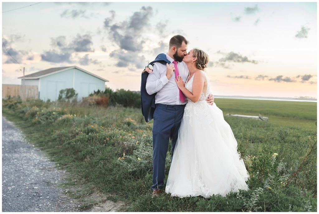Couple sharing romantic kiss at sunset in open field on their wedding day.