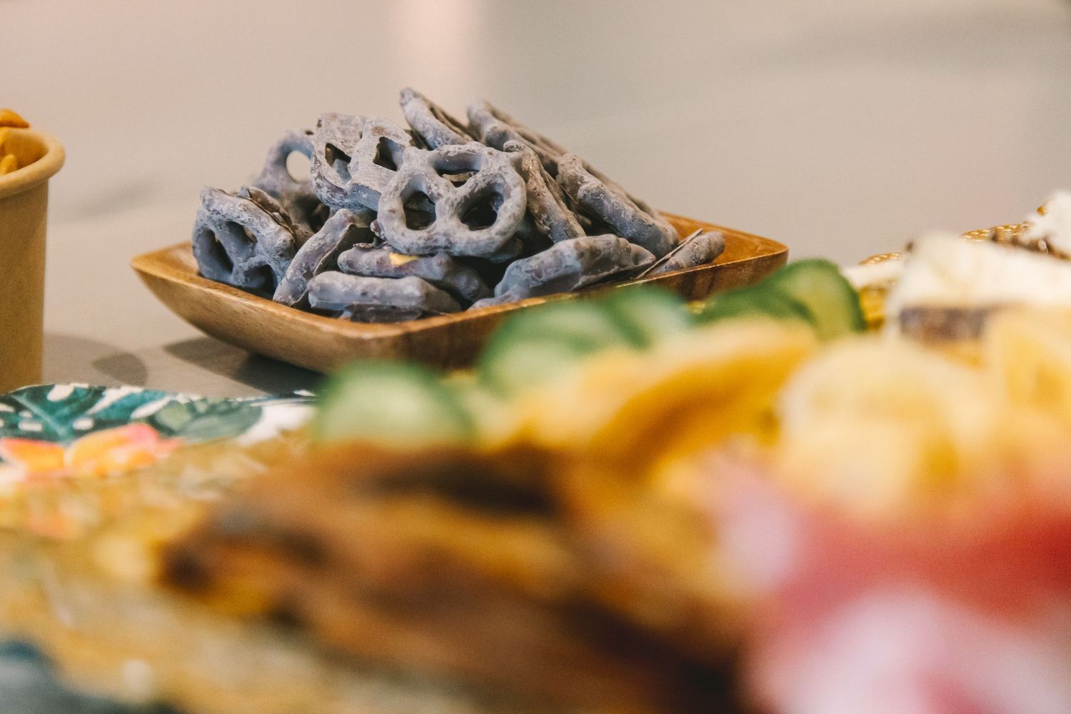 Chocolate-covered pretzels displayed on a wooden board at a wedding reception snack table.