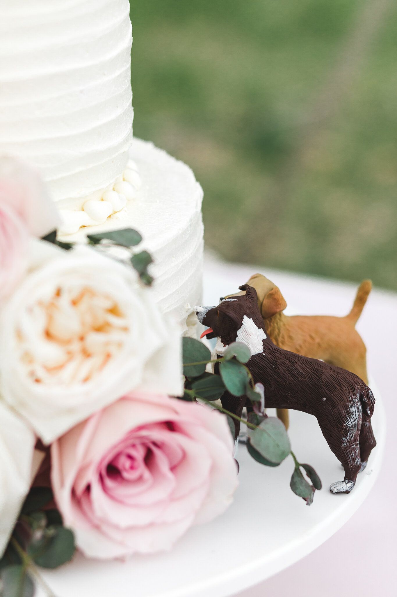 Elegant white wedding cake with pink roses and playful dog figurine cake toppers.