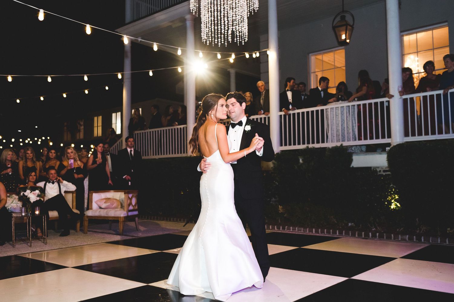 Bride and groom sharing their first dance on a black and white checkered outdoor dance floor at night.