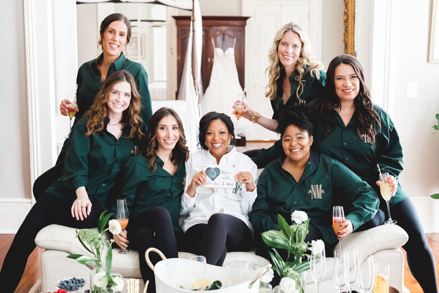 Bridesmaids in matching green velvet robes celebrate with champagne while posing with the bride during wedding preparations.