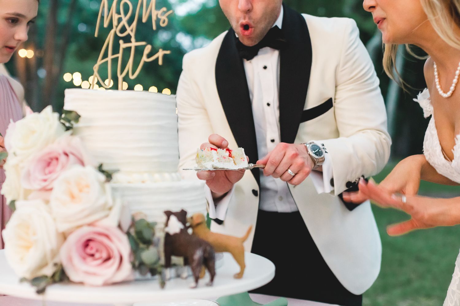 Bride and groom cutting a white wedding cake decorated with pink roses and a Mr. and Mrs. cake topper.
