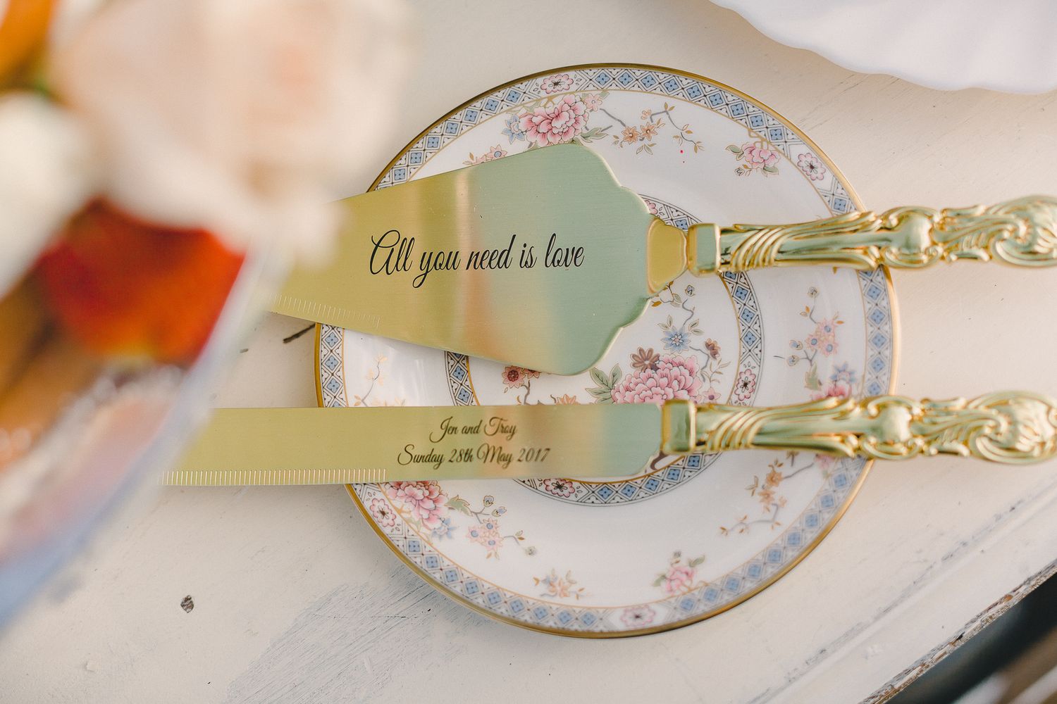 Gold cake serving set with All You Need Is Love ribbon on vintage floral china plate.