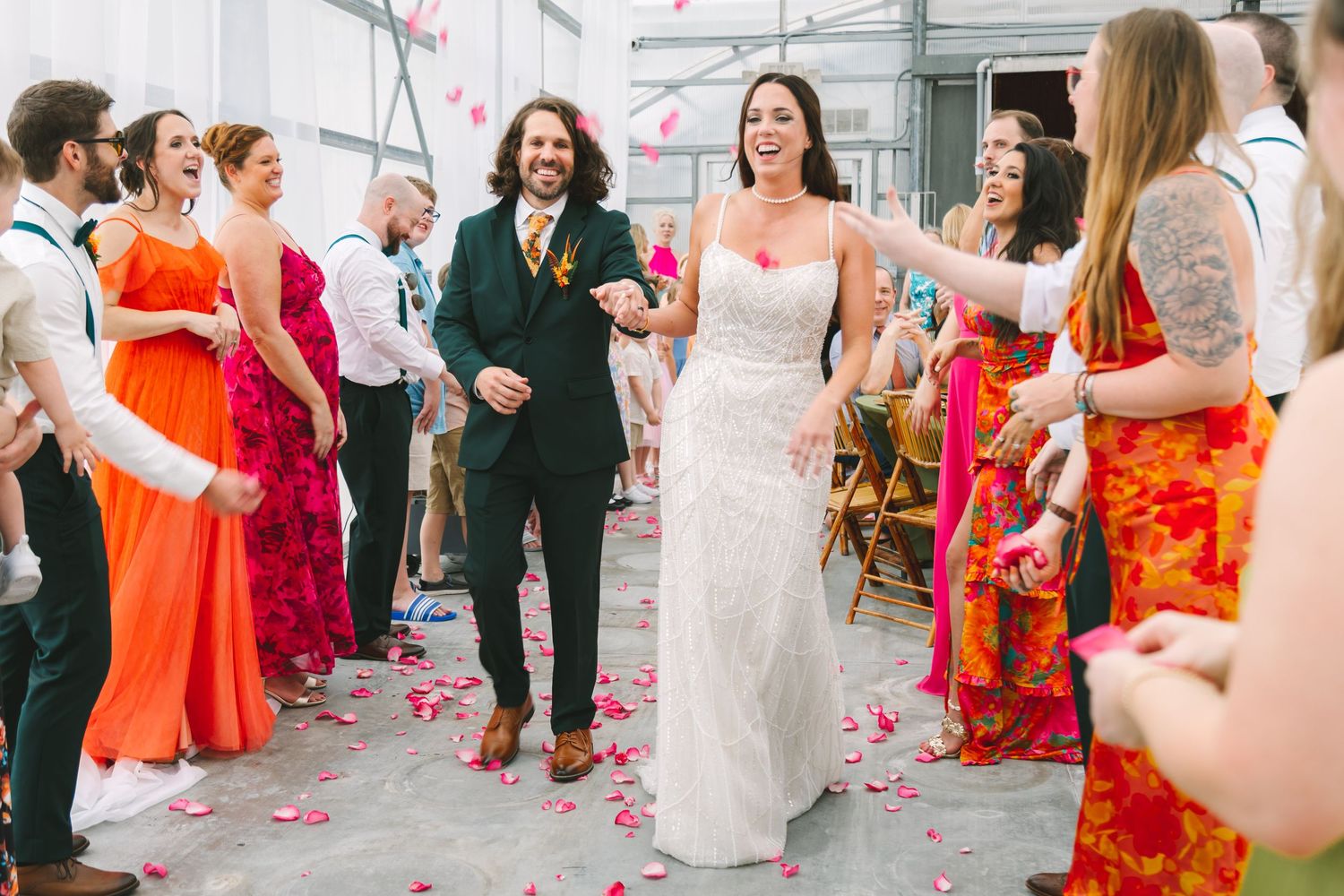 Bride and groom walk through petal toss at colorful indoor wedding reception with guests in vibrant attire.