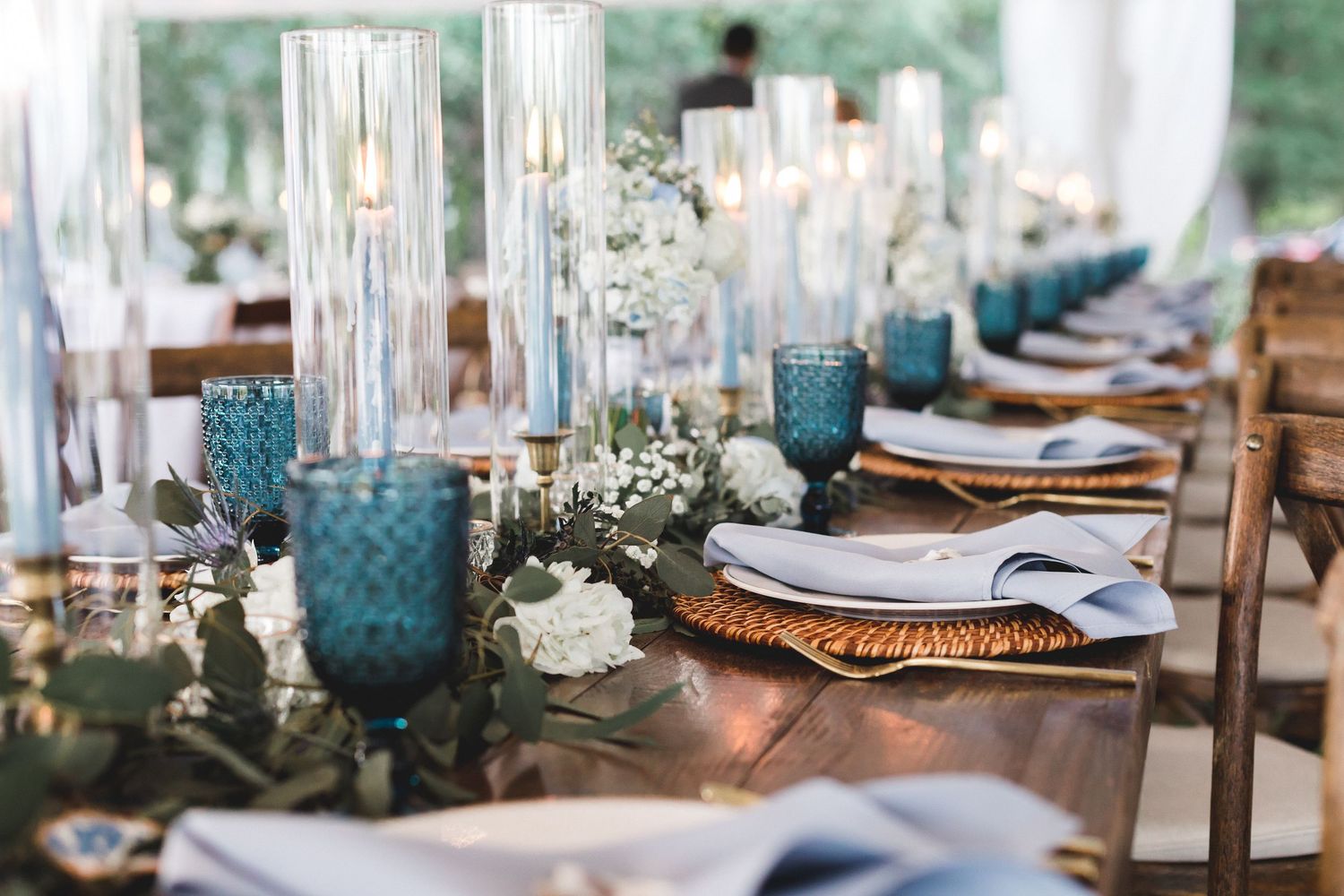 Rustic wedding reception table with blue glassware, candles, and greenery garland centerpiece.