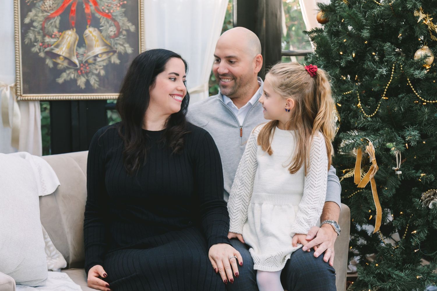Family of three smiling together near a Christmas tree during a festive holiday photo session indoors.