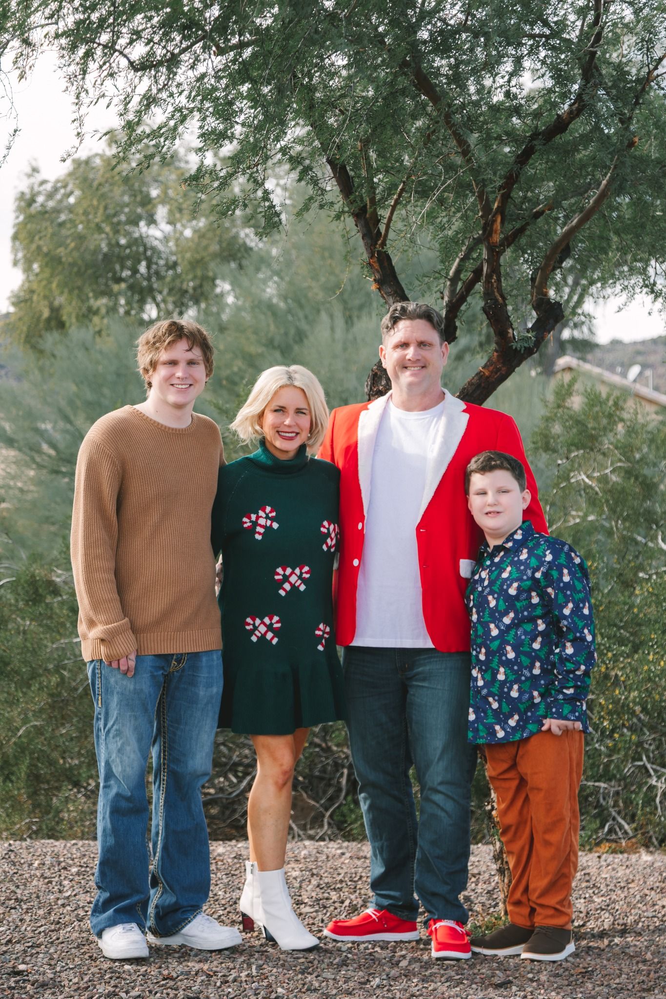 Family of four smiling outdoors under a tree, wearing festive holiday outfits in red and green.