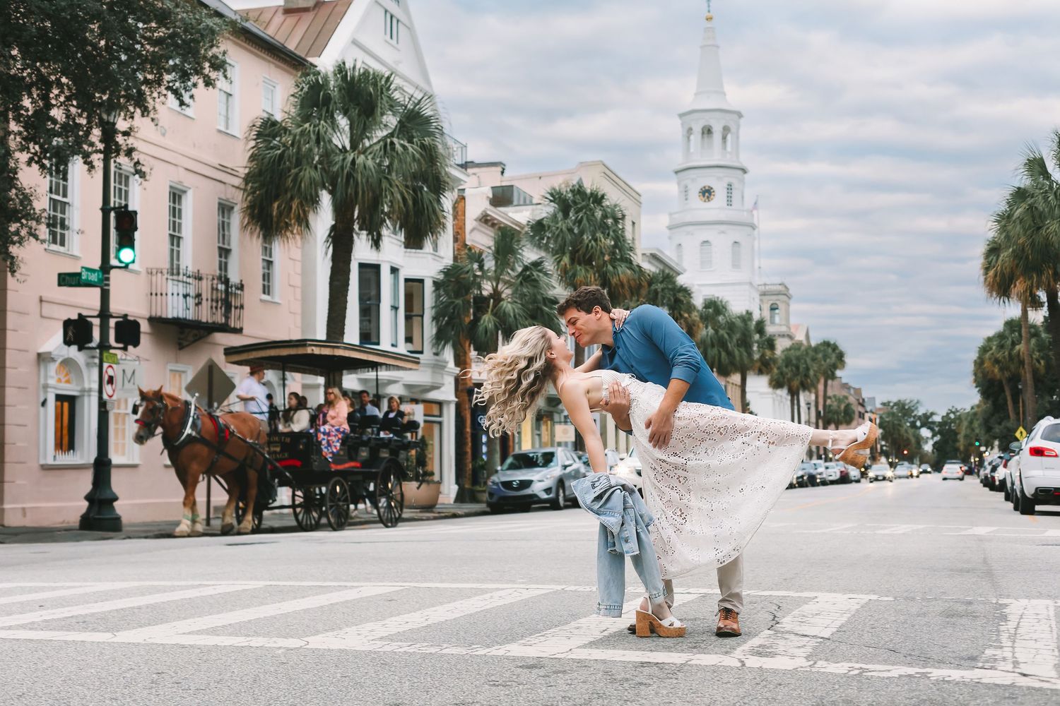 Couple sharing a romantic dip kiss on a historic Charleston street with horse carriage in background.