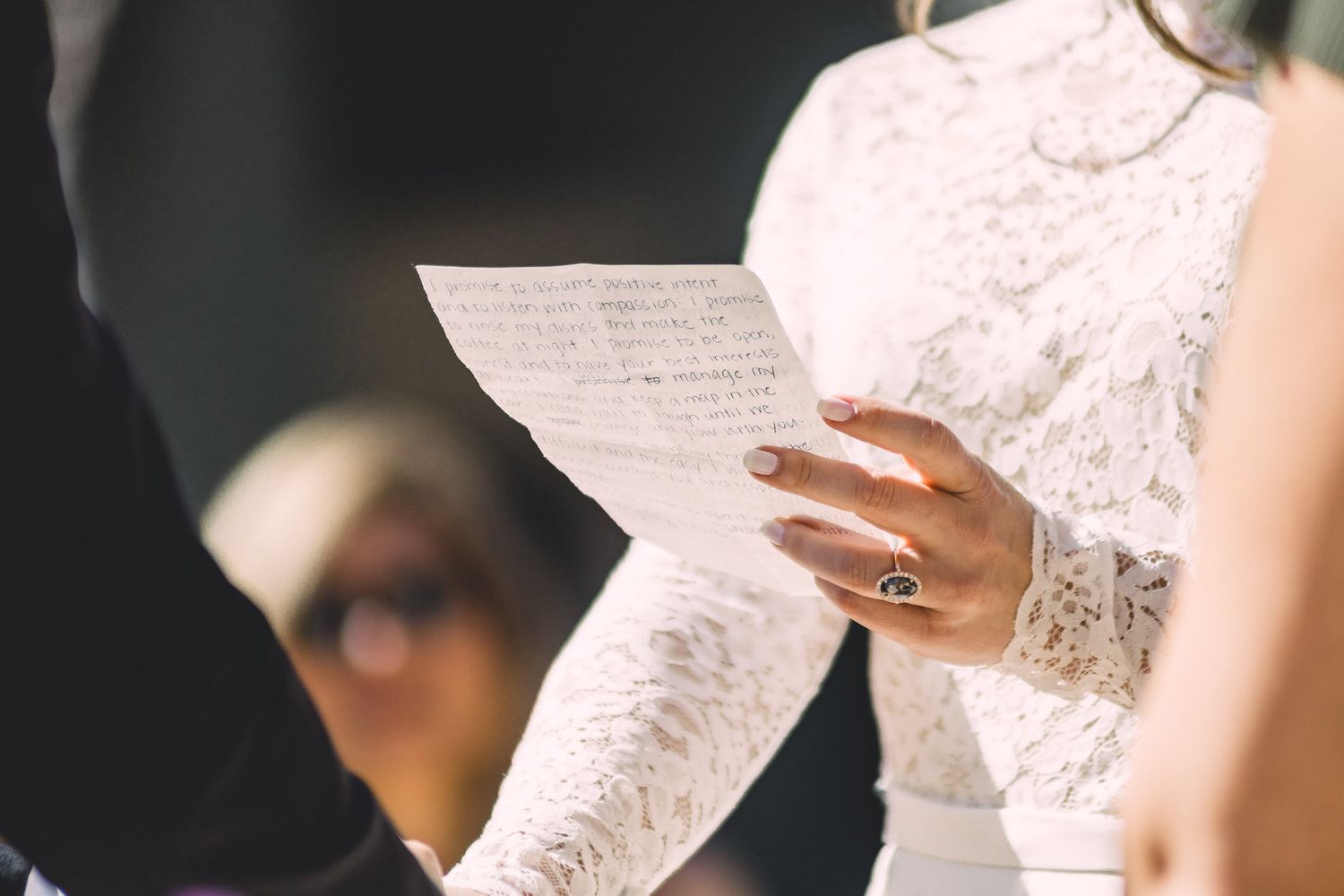 Bride in lace gown reading handwritten wedding vows during an intimate ceremony.