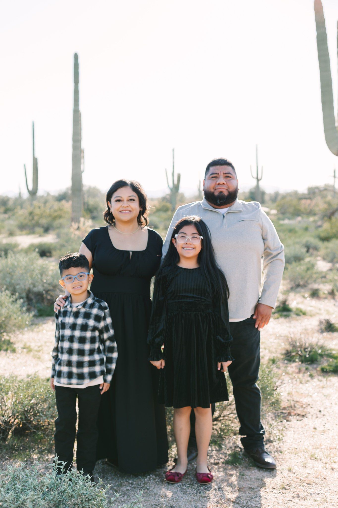 Family of four posing in a desert landscape with tall saguaro cacti in the background.