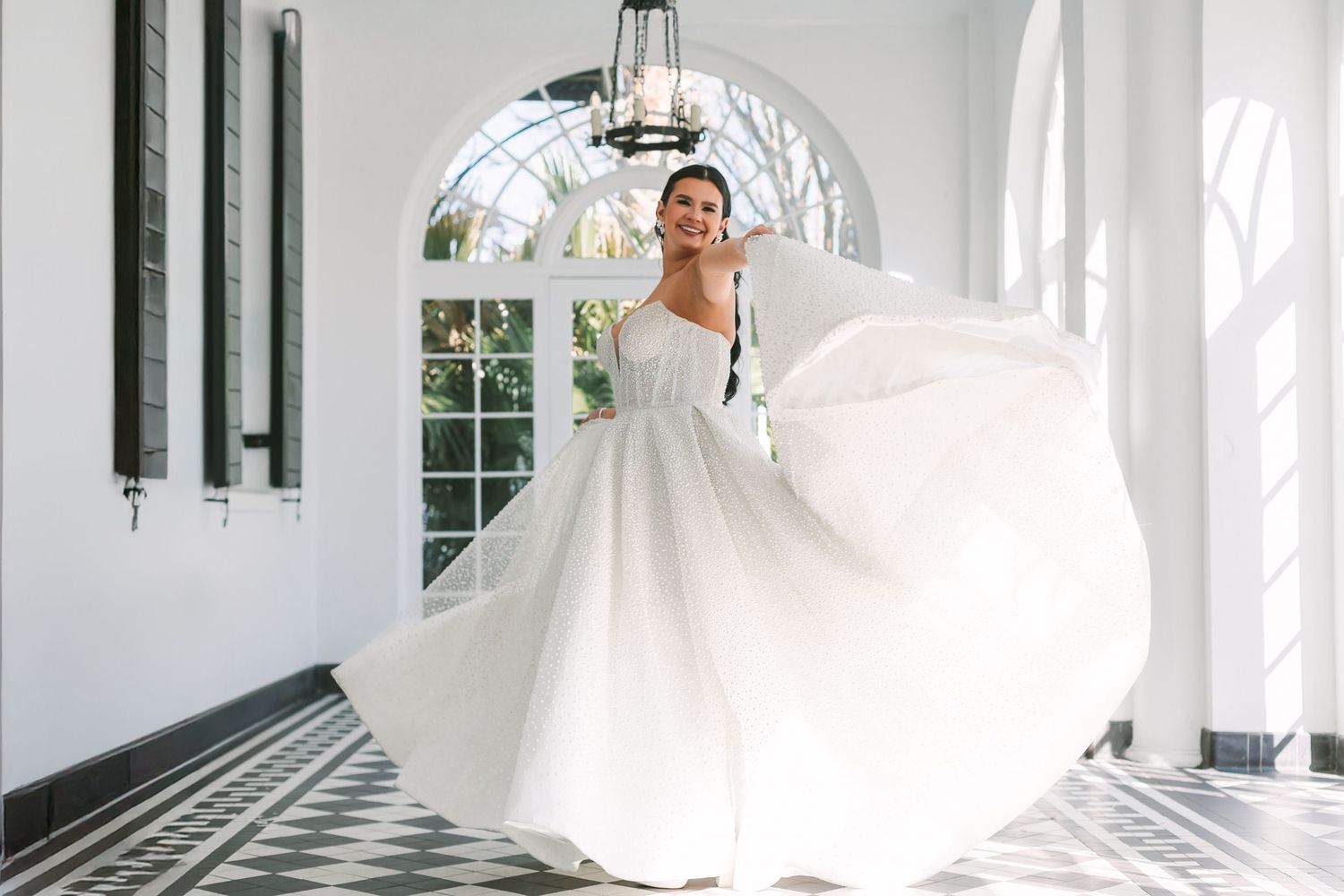 Bride twirling in a flowing white ball gown in an elegant white columned hall with black and white floors.