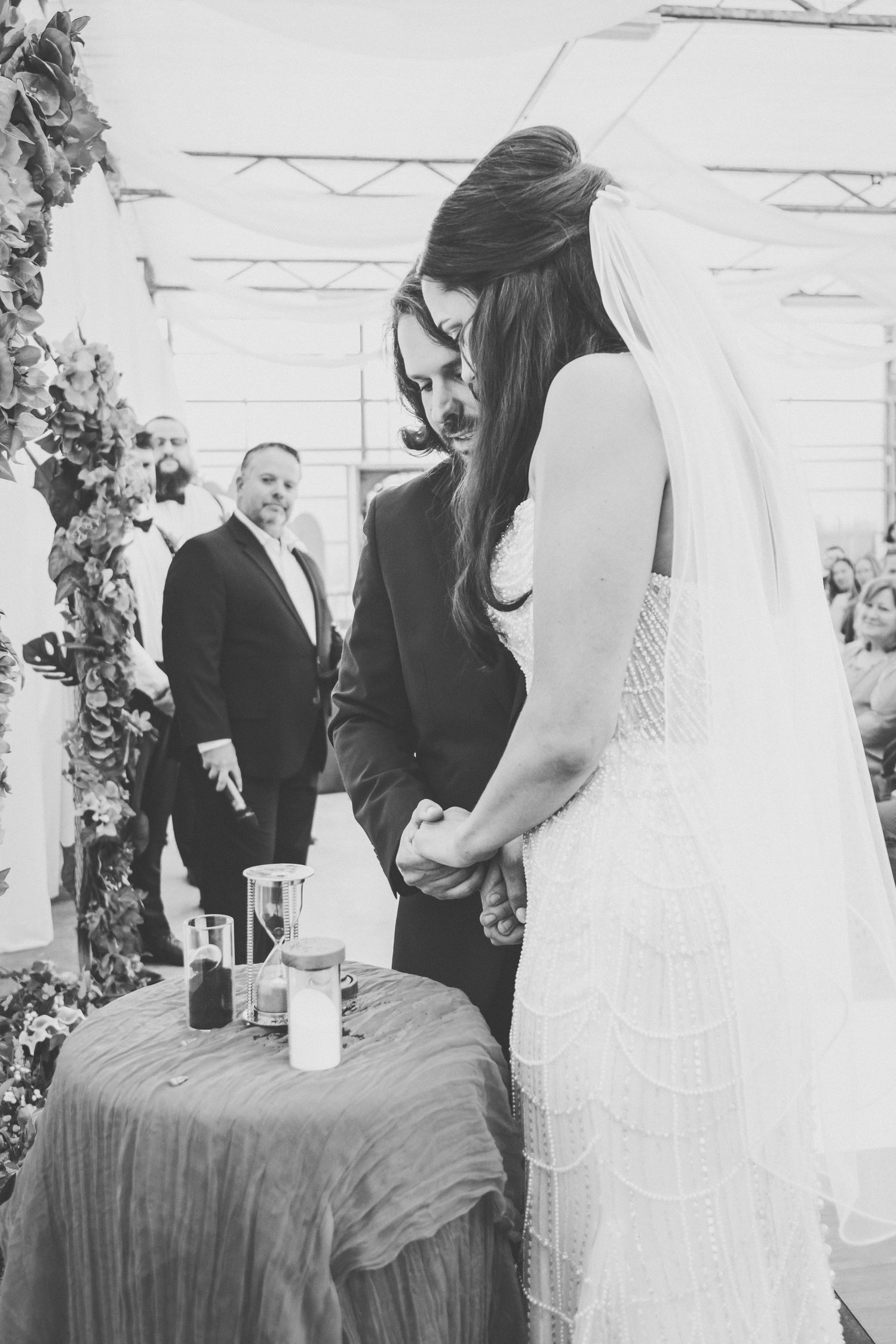Bride and groom perform sand unity ceremony at wedding altar in elegant black and white photograph.